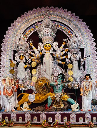 Durga kills Mahishasura with her lion (here, a white lion). Goddess Lakshmi and Ganesha are on the left and Goddess Saraswati and Kartikeya are on the right