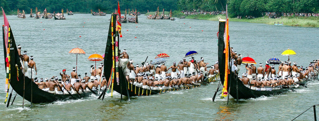 "Colorful Aranmula Palliyodams racing on the Pampa River, with enthusiastic rowers and spectators cheering from the banks"