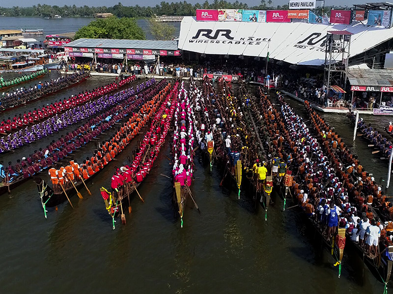 "Colorful Aranmula Palliyodams racing on the Pampa River, with enthusiastic rowers and spectators cheering from the banks"