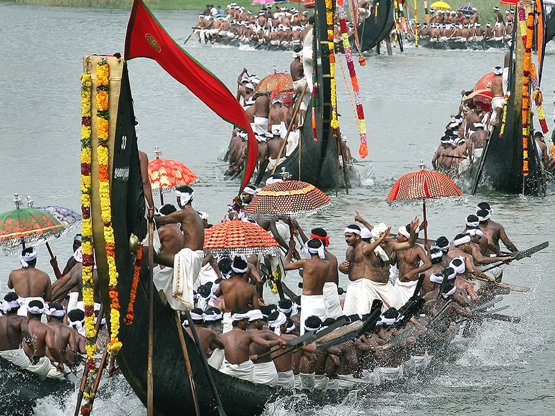 "Colorful Aranmula Palliyodams racing on the Pampa River, with enthusiastic rowers and spectators cheering from the banks"