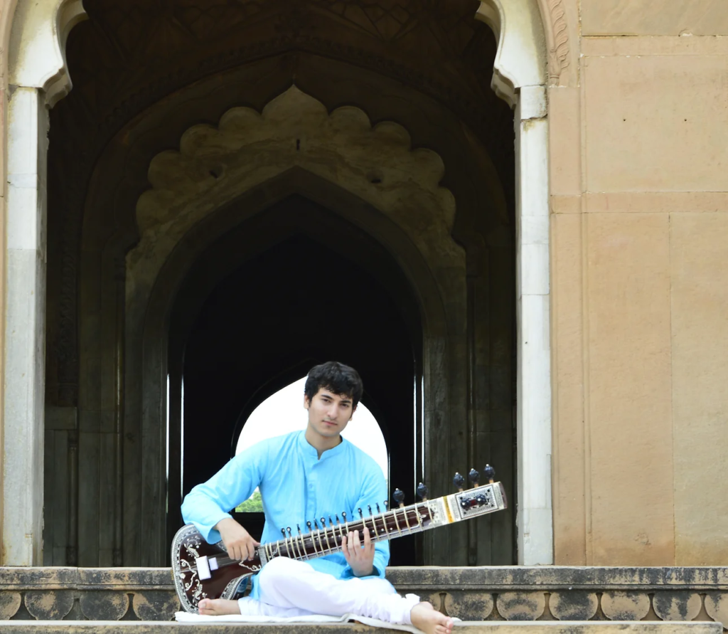 Rishab Rikhiram Sharma passionately performing on the sitar during a live concert, with vibrant stage lights illuminating the scene, symbolizing his dedication to music and mental health advocacy.