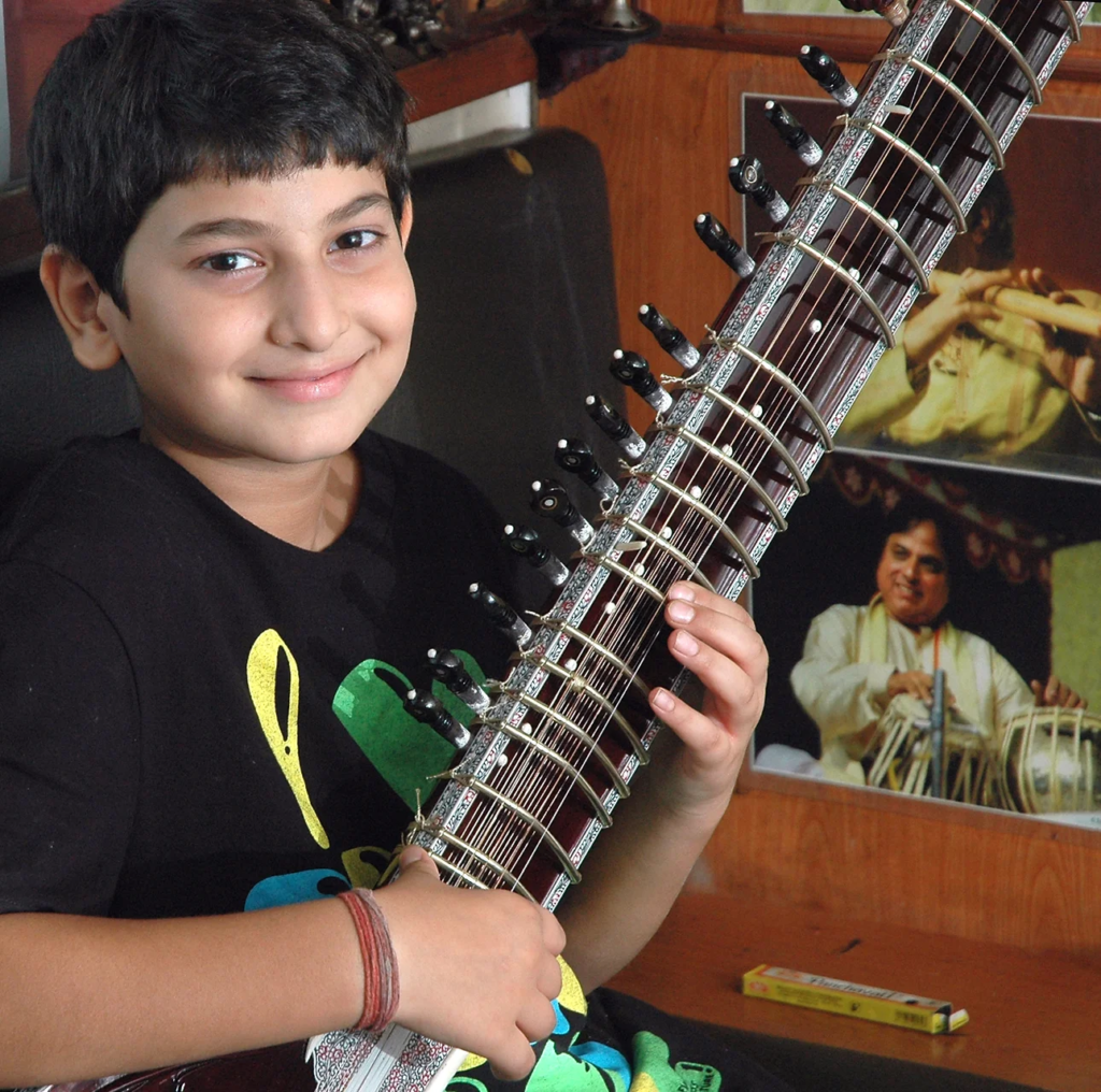 "Young Rishab Rikhiram Sharma smiling while playing the sitar, showcasing his early passion for music."