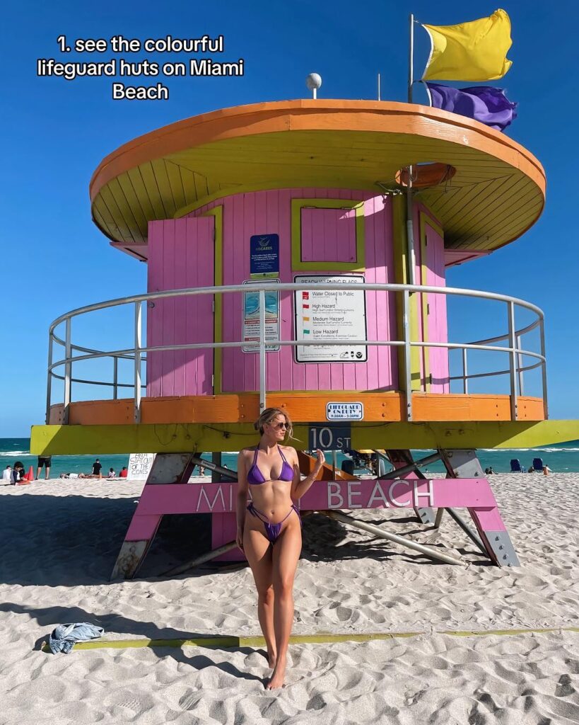 A vibrant pink and lime green lifeguard tower on Miami Beach, set against a clear blue sky and sandy shore.