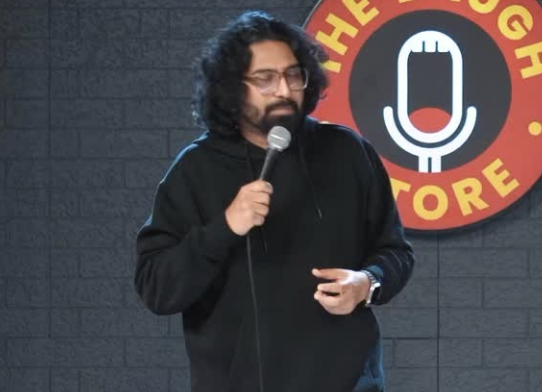 "Ravi Gupta comedian performing energetically on stage with a microphone, smiling under a spotlight with a cheering crowd in the background, featuring bold text 'Comedy King!' in a vibrant red and yellow design."